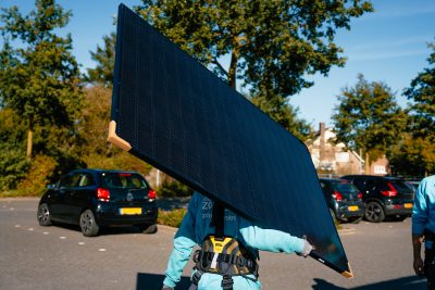 100% Zonnig monteur loopt met een zonnepaneel op zijn arm naar projectlocatie